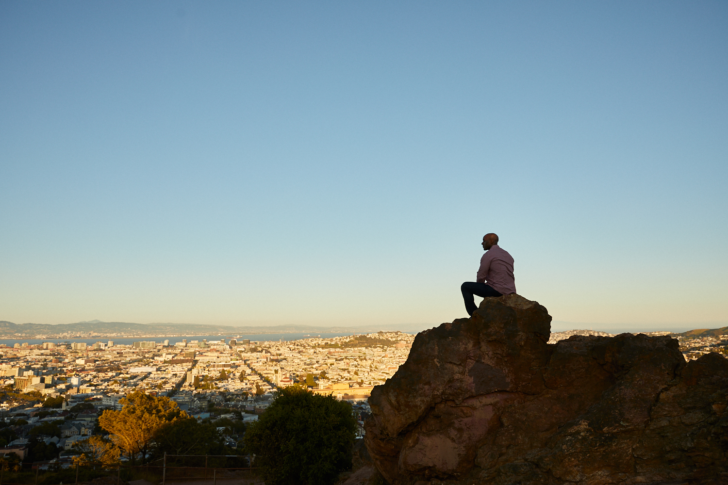 man sitting on rock with overview of city